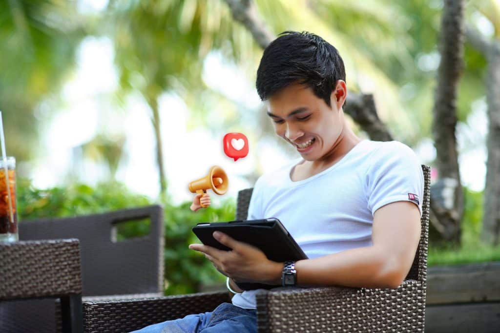 A person is smiling while looking at images of a clean landscaping project on the tablet in their hands. Emojis are floating in the air next to them.