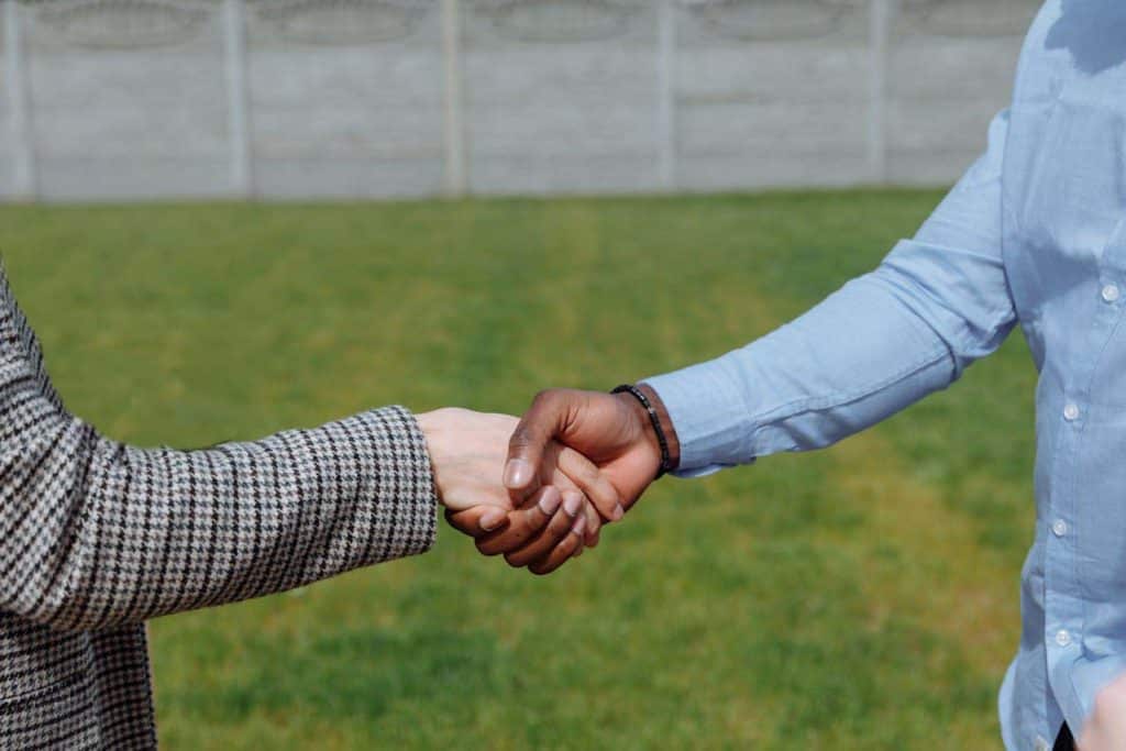 A lawn care specialist and a homeowner shake hands in the homeowners front yard.