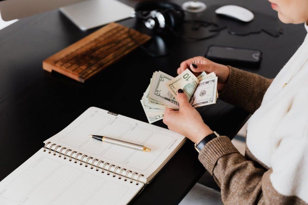 A landscaper is sitting at a desk, counting money over their open business planner.
