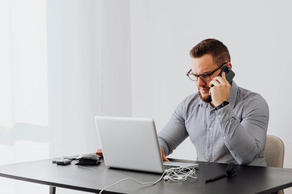 A person sits at a desk in front of their open laptop, talking on the phone about a landscaping project.