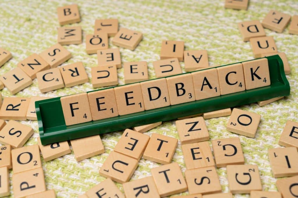 Small wooden letters picked from a pile and arranged on a green tray to spell out 'FEEDBACK'