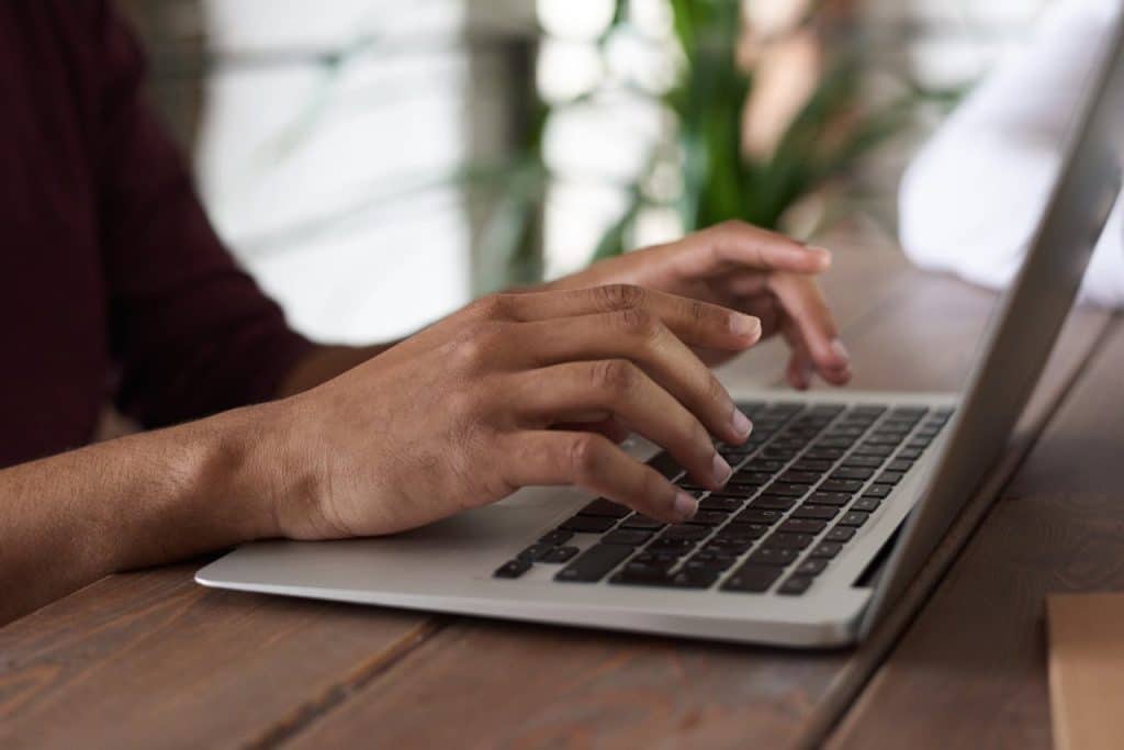 Two hands typing on a laptop that is sitting on a desk.