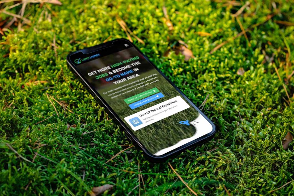 A cellphone laying in grass, displaying a marketing website for lawn and landscaping companies.