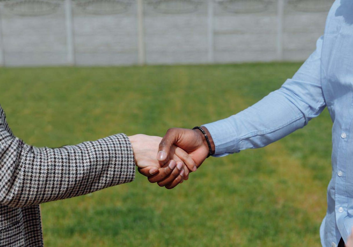 A lawn care specialist and a homeowner shake hands in the homeowners front yard.