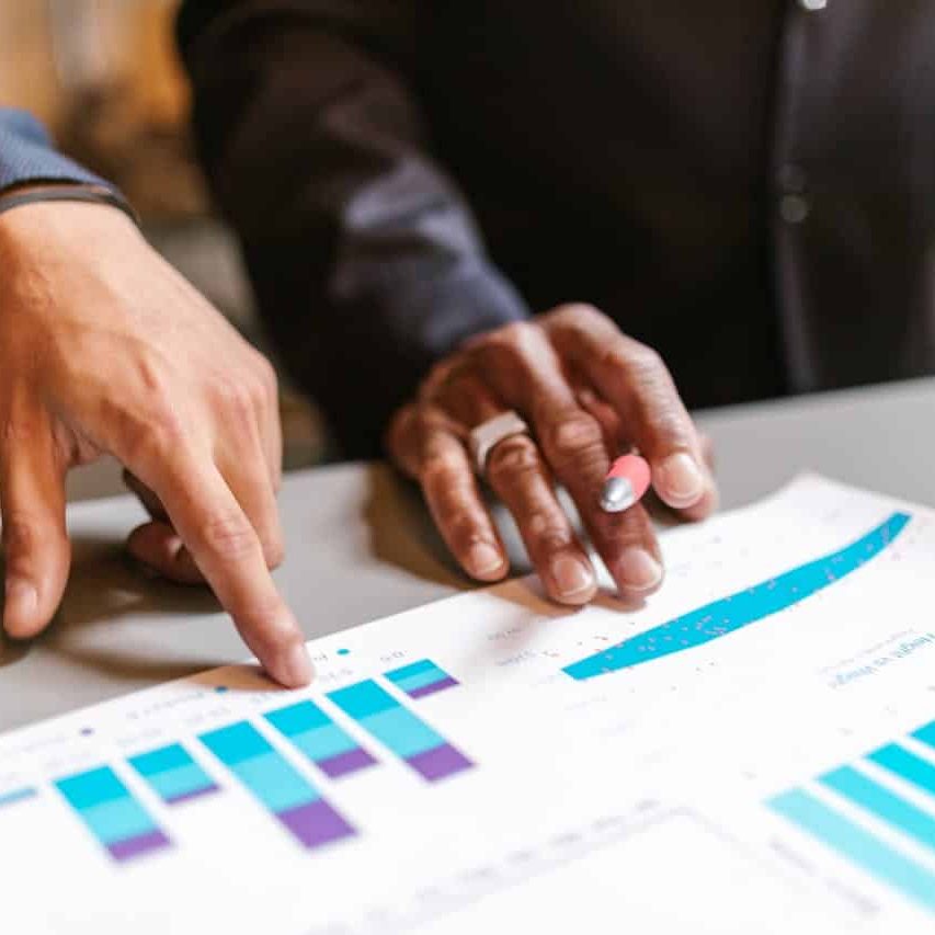 Two landscape business owners analyze a document with bar charts on ROI of landscaping services. One person is holding a pen, the other is pointing at the document.