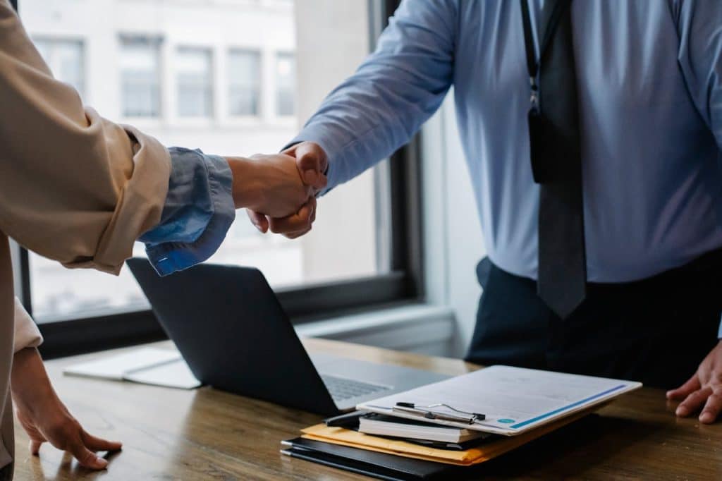 A landscape business owner and a client are shaking hands over a desk after completing a successful project.